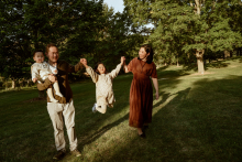 In a Toronto park, this family moves through the evening light with playful energy as one child swings joyfully between her parents. The long shadows and open green space give the photograph warmth, movement, and genuine family connection.