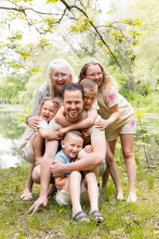 A playful family piles together with laughter beside a peaceful pond during a relaxed outdoor lifestyle session in Overijssel, Netherlands.