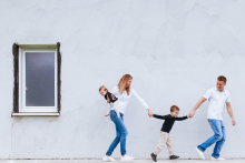 A family walks playfully together while holding hands beside a simple white wall during a lifestyle session in Bardos, Pyrénées-Atlantiques, France.