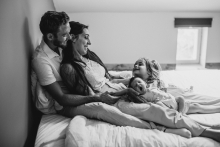 A family relaxes together on a bed as their young daughter laughs beside her sleepy baby sibling in Loire, France.