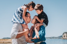 A family of four shares a playful embrace with the children perched on their parents’ shoulders at the beach in Toulon, France.