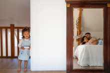 A young girl stands nearby while her parents cuddle together on their bed, awaiting a new baby in Indre, France.