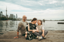 A family shares time together on a waterfront dock with the Toronto skyline rising behind them.