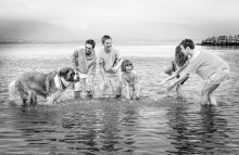 A family and their dog play together in the shallow bay waters during a relaxed outdoor family session in Chéticamp, Nova Scotia, Canada.