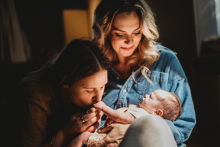 A mother cradles her newborn while her partner gently kisses the baby’s tiny foot during an intimate family moment in Boston.