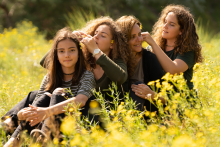 A mother and her three daughters sit together among wildflowers, playfully arranging flowers in each other’s hair in Vogelenzang, the Netherlands.