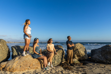 A family gathers among sunlit rocks along the shoreline, overlooking the ocean during a lifestyle photography session at Venice Beach, California.