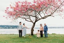 A multigenerational family gathers beneath a blooming cherry blossom tree beside the waterfront during a spring lifestyle session in Seattle.