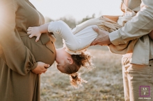 Capturer des moments d'amour et de joie : un doux portrait de famille dans l'Oise, France Dans un champ ensoleillé de l'Oise, en France, une jeune fille est suspendue la tête en bas dans les bras de son père. Avec des baisers affectueux, elle adore le ventre de femme enceinte de sa mère, créant un beau moment de chaleur et d'amour.
