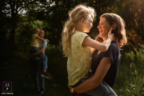 Mother and daughters in Haute-Garonne, France are back-lit by the sun in a forest. The light on the edges of their hair and clothing creates a warm and loving portrait of their close bond.