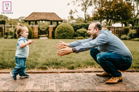A toddler is walking toward their crouching dad on a sidewalk at Waveny park. The child's arms are outstretched, as if saying "Daddy, I'm coming!"