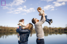 In Lyon, France, a family portrait features parents standing back to back, each joyfully lifting a child into the air. The scene radiates happiness, closeness, and playful energy.