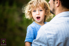 In Cupertino, California, a father holds his young son for a family portrait. The boy gazes at the camera with an inquisitive expression, as they are together in a peaceful outdoor setting.