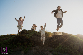In San Francisco, CA, a family joyfully leaps off sand dunes together, capturing playful energy and fun as they jump in unison against the sandy, coastal landscape.