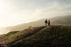 In Marin, CA, a family hikes along the ridge of a hill, dramatically backlit with beautiful Mt. Tamalpais in the background. Silhouetted figures create a scenic, adventurous outdoor scene.