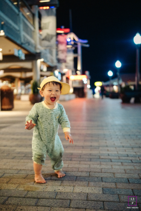 At Redondo Beach, California, a one-year-old stands tall for the first time, immersed in pure delight during a nighttime urban photo.