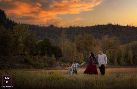 Golden Hour Family Stroll: Portland Sunset Glow Amidst Peaceful Grassland In Portland, Oregon, a family walks through a field of low grass at sunset, surrounded by warm light and a peaceful landscape.