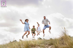Overijssel Sand Dune Leap: Joyful Family Portrait Of Four Capturing Fun Movement In Overijssel, Netherlands, mom, dad, and two kids leap together across the sand dunes, their expressions full of joy during a family portrait session.