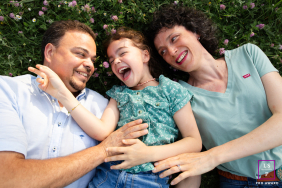 Photo by: <a href="https://www.lifestylephotographers.com/lifestyle-photography-portraits/anais-bertrand/toulouse/2096293">Anais Bertrand - France</a> In Haute-Garonne, France, a joyful family—mom, dad, and child—lie on their backs in the grass, smiling up in a scene of pure happiness.