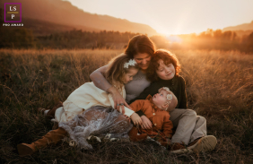 Golden Sunset Snuggles: Family Embracing Warm Light on Portland Hillside In Portland, Oregon, a family snuggles together on a hillside at sunset, backlit by warm, golden light.