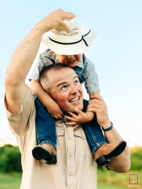 In Harlingen, Texas, a father places a cowboy hat on his son's head as the boy sits on his shoulders outdoors.