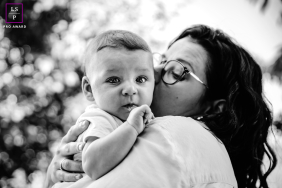 Isère, France: A Mother's Tender Embrace, Toddler's Gaze, Timeless Black-and-White In Isère, France, a black-and-white portrait shows a mother holding her toddler against her chest, the baby looking directly at the camera.