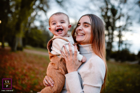 Mother and Child Sharing Joyful Laughter Outdoors in French Isère Woodlands In Isère, France, a mother holds her joyful toddler outdoors, both laughing and smiling, surrounded by trees.