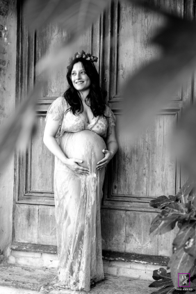 Outside an ancient wooden door in Meldola, Italy, a black-and-white portrait features an expectant mother adorned with flowers in her hair.