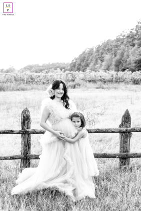 In the countryside near Meldola, Italy, an artistic black-and-white portrait features an expectant mother and her first child in a field beside a wooden fence.