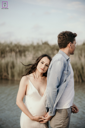 At Ravenna Wildlife Sanctuary in Italy, a candid maternity portrait shows a couple embracing in nature; he faces away as she nestles into his back, smiling warmly at the camera.
