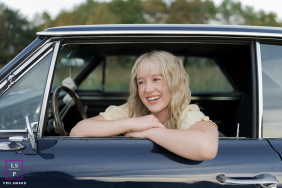 In West Bend, Wisconsin, a teenage girl sits in the driver’s seat of her grandpa’s vintage car, leaning out the window and smiling brightly.