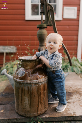 In Richfield, Wisconsin, a toddler beams at the camera with excitement after discovering a jug filled with water, his joyful expression capturing his love for play.