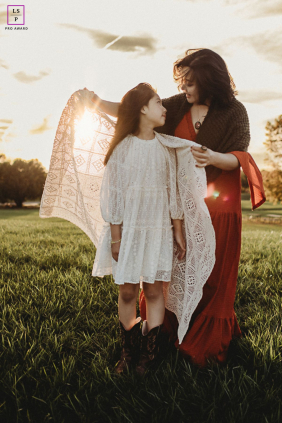 Golden Sunlight Hugs: Oakville Mother's Warmth And Daughter's Affection In Oakville, Ontario, golden sunlight streams from behind as a mother wraps her daughter in a blanket, their faces softly illuminated with warmth and affection.