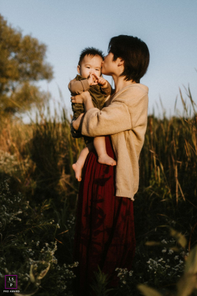 Golden Sunset Kiss, Markham Mother Lifts Young Son In Tender Embrace In Markham, Ontario, a mother lifts her young son and kisses his cheek during a golden sunset, capturing a tender, sunlit embrace.