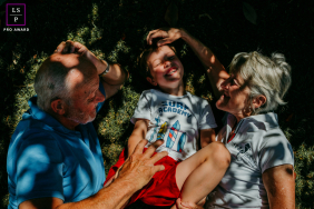 Mauguio Grandparents And Grandson Sharing Laughs And Sunlight Dappled Tickles Outdoors In Mauguio, France, grandparents and their young grandson share laughs and tickles outdoors, sunlight dappling their faces.