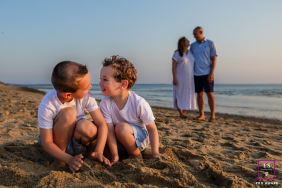 Laughter Shared By Siblings, Watched By Parents, On Chatham Beach Sand At Chatham Beach in Chatham, Massachusetts, two siblings share laughter in the foreground while their parents watch from behind, the scene capturing the lightness and authenticity of childhood.
