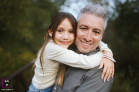 San Diego Dad Hugs Daughter, Cheek To Cheek, Affectionate Expressions Captured In San Diego, California, a dad hugs his daughter cheek to cheek, both looking at the camera with close, affectionate expressions.