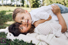 Laughter And Love In Lyon: Mother And Son Lying In Grass In Lyon, France, a mother and son lie together in the grass, the son atop his mother, both looking at the camera and laughing.