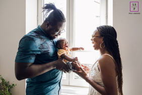 French Laughter: Dad Holds Baby Facing Mom In Lyon Embrace In Lyon, France, dad holds his baby as the little one laughs loudly, facing mom who smiles back at them both.