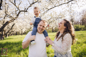 Lyon Family Laughs, Cherry Blossoms Bloom, Son On Father's Shoulders In Lyon, France, a family poses among cherry blossoms, their son on his father's shoulders as they all laugh together.