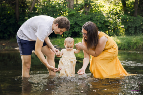 Lyon Family Splash: First Year Celebrated Gently In The Brook Water In Lyon, France, mom and dad gently play with their one-year-old daughter in the brook water, celebrating her first experience splashing together as a family.