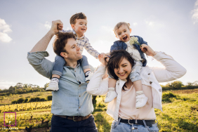 Lyon Family Laughing Loudly: Dad And Mom Shoulder-Carry Their Children In Lyon, France, dad carries son on his shoulders while mom carries daughter on her shoulders, the whole family laughing loudly together.