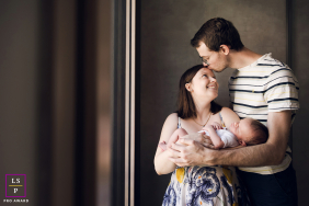 Tender Embrace Of Newborn Baby Family Portrait In Lyon, France In Lyon, France, a newborn portrait features mom cradling her baby in her arms as dad embraces them both, gently kissing her forehead.