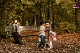 Toronto Autumn Afternoon: Dad Hugs Children, While Mom Rests Nearby In Toronto, Ontario, a family enjoys an autumn afternoon; mom sits on a wooden bench in the background while dad hugs their two children in the foreground.