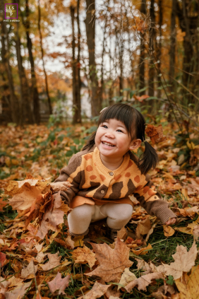 In Toronto, a girl dressed in fall colors picks up maple leaves, surrounded by autumn’s vibrant foliage.