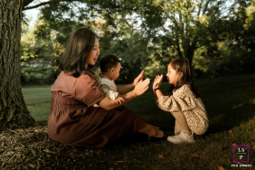Toronto Mother And Daughter Hand-Clapping Game Under Illuminated Tree Shadows In Toronto, Ontario, a mother and daughter play a hand-clapping game beneath a tree, sunlight illuminating them as shadows from the branches surround nearby.