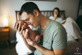 New Dad Gently Connects Head To Head With Newborn Baby In Queens In Queens, New York City, a dad gently goes head to head with his newborn baby during an in-home family session, with mom in the background.