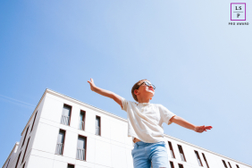 Joyful child airborne, running with arms outstretched, against a bright background in Bayonne, France.
