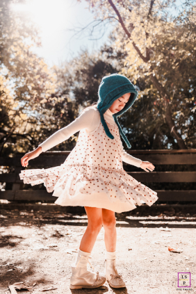 Joyful young girl twirling her dress while playing happily in a sunny Hayward park.