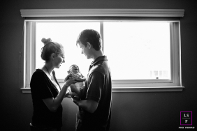 Softly Lit Black And White Family Portrait With Parents And Newborn Baby Black and white family portrait: parents lovingly hold their newborn baby, softly lit by bright natural window light.